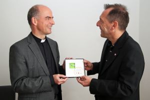 Bischof Dr. Franz Jung (links) erhält von DAHW-Geschäftsführer Burkard Kömm ein Stück Original-Tornetz vom Spiel Deutschland gegen Brasilien bei der Fußballweltmeisterschaft 2014.
