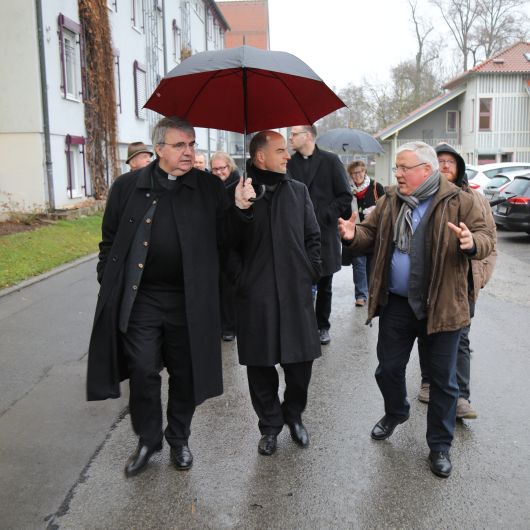 Albrecht Euring (rechts), Leiter des Simonshofs, führte Bischof Dr. Franz Jung (Mitte) durch die Einrichtung. Domkapitular Clemens Bieber sorgte dafür, dass der Regen nicht den Bischof erwischte. 