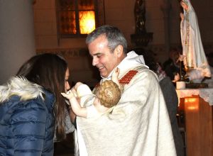 Padre Dr. Joaquim Carneiro da Costa hält nach der portugiesischen Tradition die Figur des Jesus Kindes während die Gemeindemitglieder nach vorne kommen und es küssen. Das Bild entstand Weihnachten 2019, vor der Corona Pandemie.