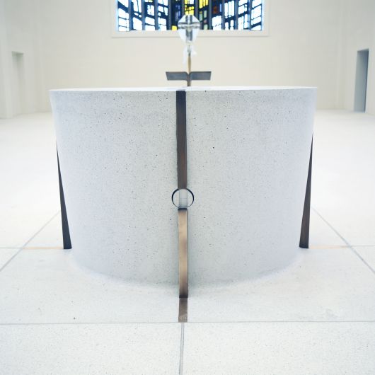 Der Altar ist aus dem gleichen Material wie der Boden und scheint buchstäblich aus diesem herauszuwachsen. Einziger Schmuck sind die senkrechten Bronzestreifen.