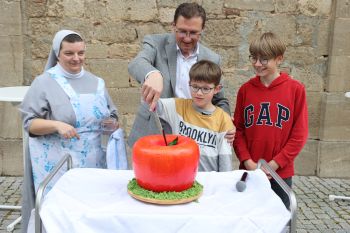 Die von Schwester Ewa Mazur (links) gebackene Torte in Apfelform schnitt Dekan Dr. Andreas Krefft mit Hilfe der beiden Brüder Laurens und Luis (rechts) Hippeli an.