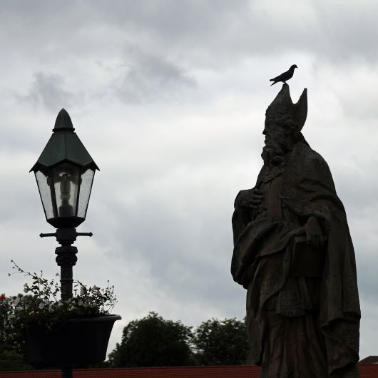 Eine Taube sitzt auf dem Kopf des heiligen Fridericus auf der Alten Mainbrücke in Würzburg. In der Kirche gilt die Taube als Symbol für den Heiligen Geist, doch die Stadttaube wird oft als "fliegende Ratte" beschimpft und verjagt.