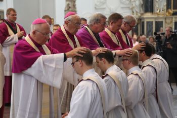 Weihbischof em. Helmut Bauer (stehend, zweiter von links) legt Paul Reder (kniend, zweiter von links) bei der Priesterweihe im Dom die Hände auf. 